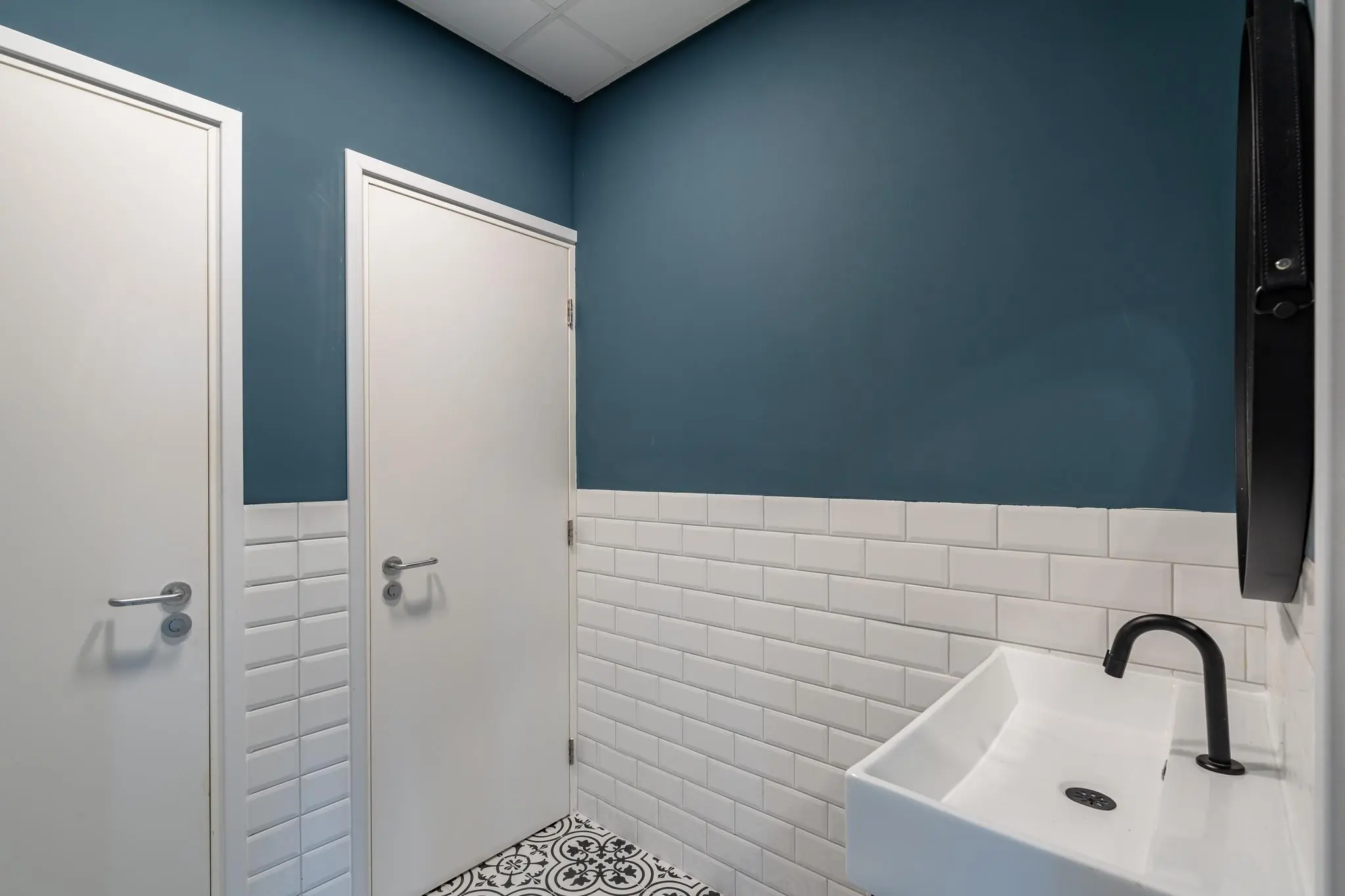 Moderne toiletruimte met twee witte deuren, een witte wastafel en een blauw-witte betegelde muur.